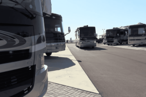 Several large recreational vehicles (RVs) are parked in designated spaces along a paved lot under a clear sky. Several large recreational vehicles (RVs) are parked in designated spaces along a paved lot under a clear sky.